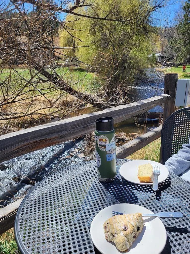 Amano Coffee + Plants seen from the path along Bear Creek — open-air seating tucked between trees with the creek running just beyond.