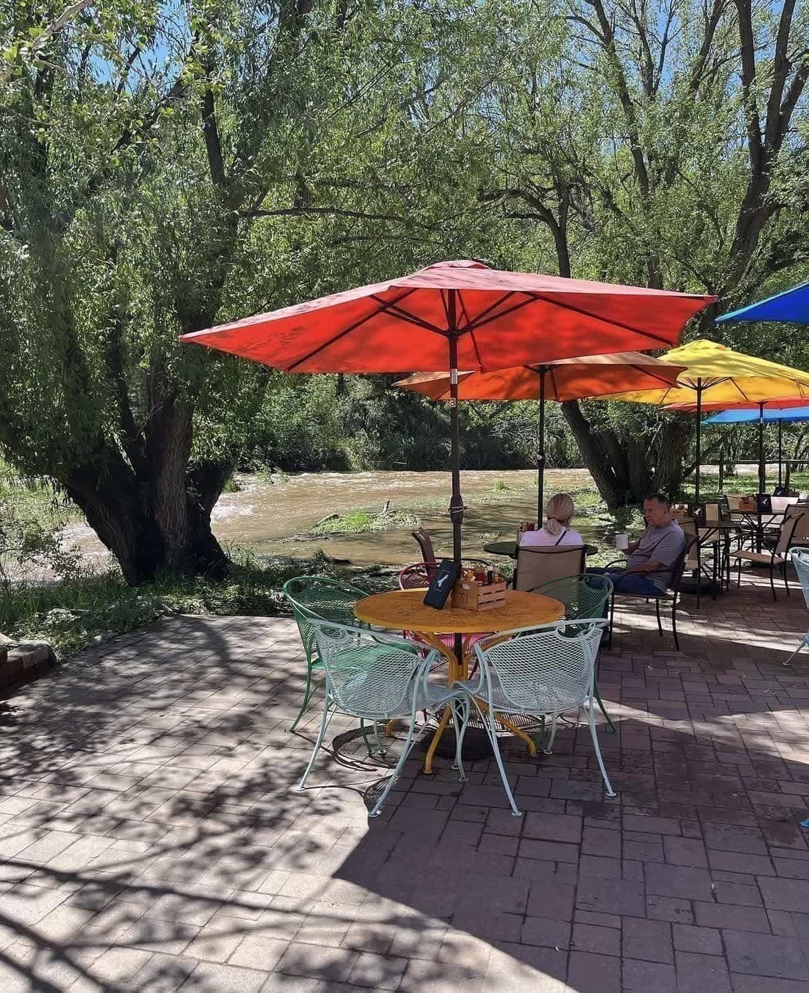 Blackbird Cafe’s creekside patio in summer — wrought-iron tables under red, orange, yellow, and blue umbrellas alongside the rushing Bear Creek.