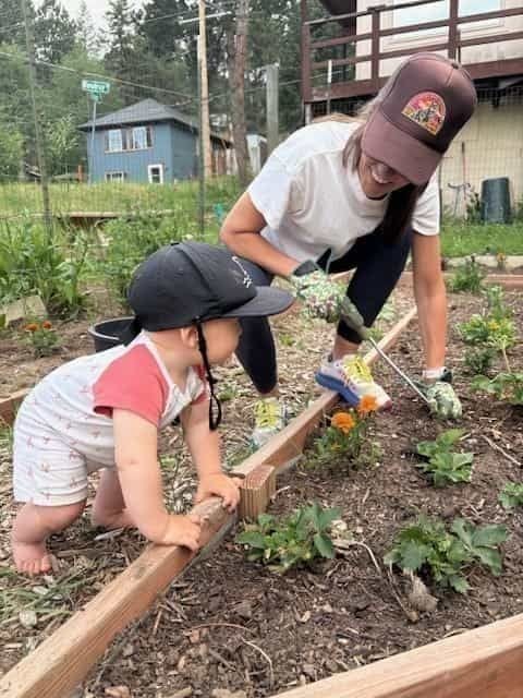 A mom and her young child planting marigolds together in a raised bed at the Kittredge community garden.