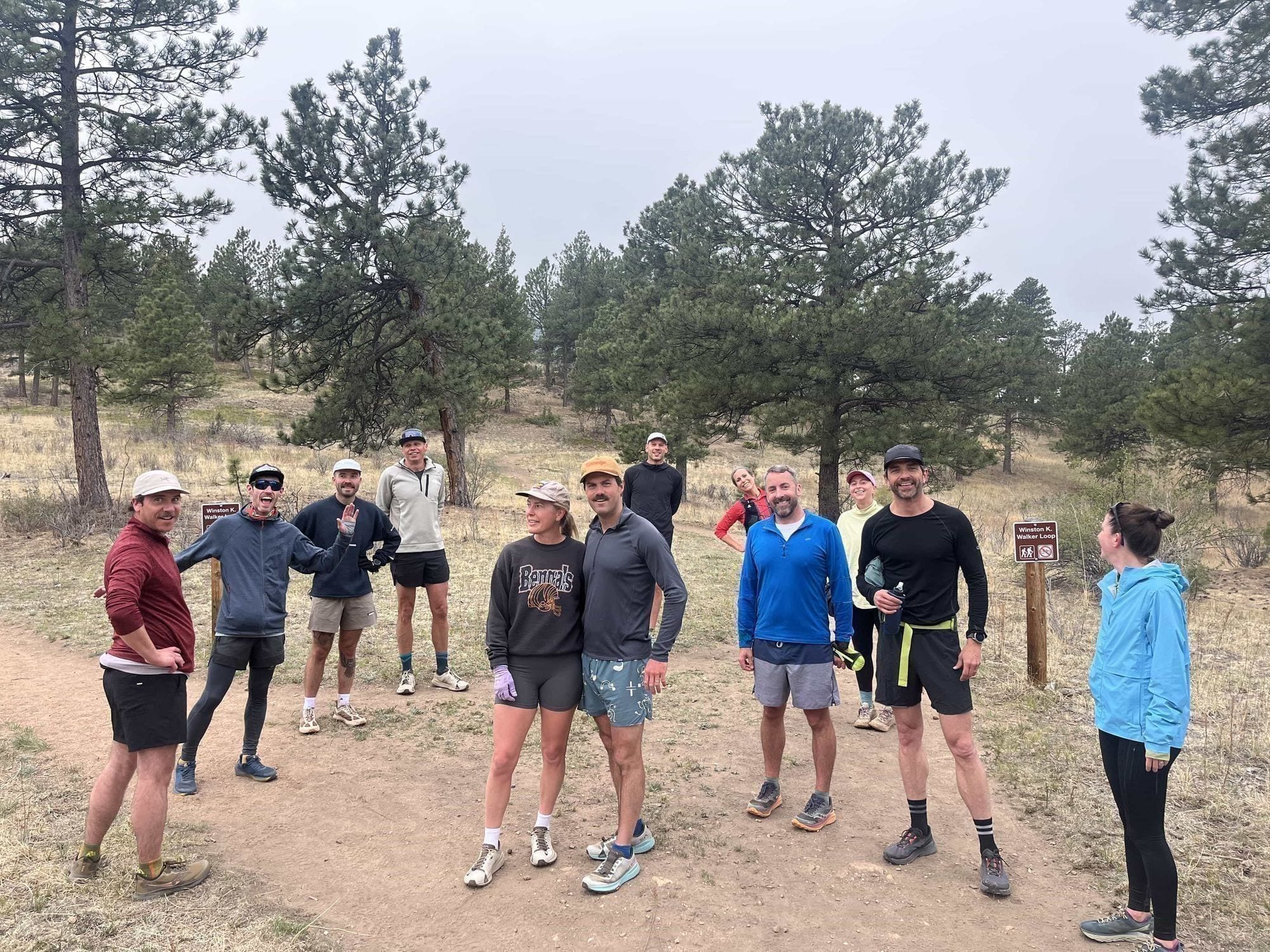 Kittredge Run Club members gathered together at a trailhead on an overcast morning, talking and laughing before a group run.