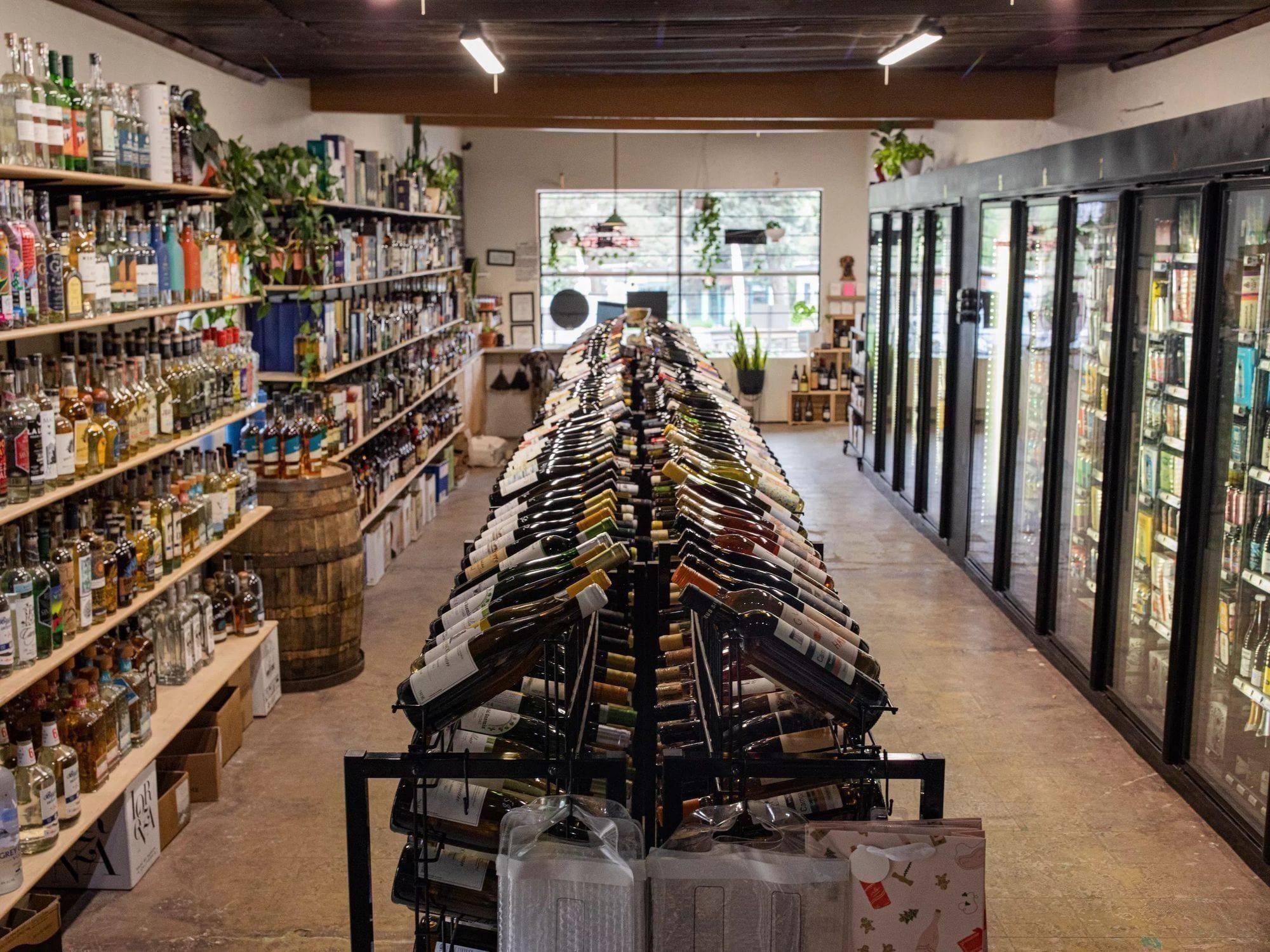 A wide aisle of wine bottles at Piney Wine & Spirits, neatly faced and labeled with handwritten staff-pick tags.