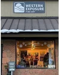 The exterior of Western Exposure Fine Art in Kittredge — cabin-style storefront with hand-lettered signage and a small bench out front.